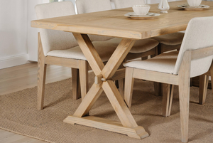 Dining table with X-shaped leg design in a room with chairs and a rug.