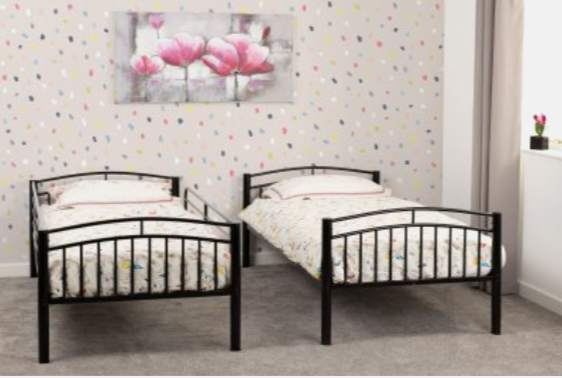 Two black metal beds in a room with colorful polka dot wallpaper.