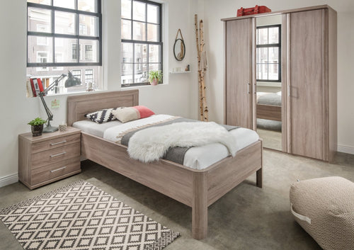 A traditional style wardrobe with a mirrored door, displayed in a bedroom setting. The wardrobe is brown and has a wooden frame, with a bed and storage drawers below.